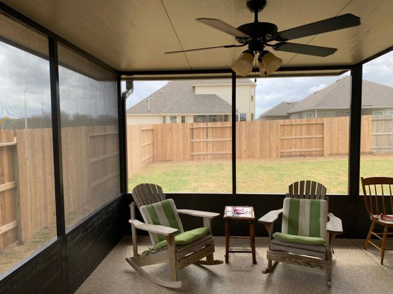 Screened-in patio with rocking chairs and table, surrounded by wooden fence.