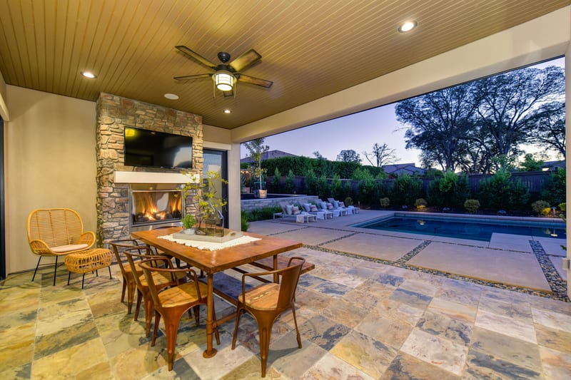 Covered patio with dining table and fireplace overlooking a pool.