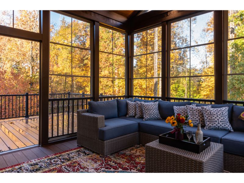 Glass patio enclosure surrounded by trees and autumn foliage.