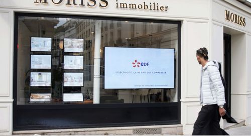 Écran digital affichant une publicité dynamique dans une agence immobilière, publicité regardé par un homme qui passe devant, ce qui illustre la captation visuelle