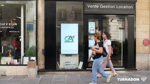 Des passants s'arrettent devant un écran vitrine attirés par la publicité dynamique proposée en devanture de commerce