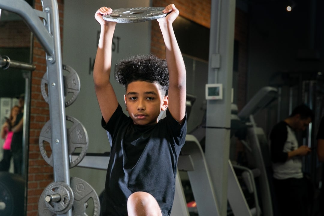 A younger child performing an overhead press with a weighted plate