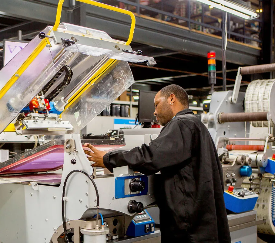 Man operating a screen printing machine in an industrial workshop.