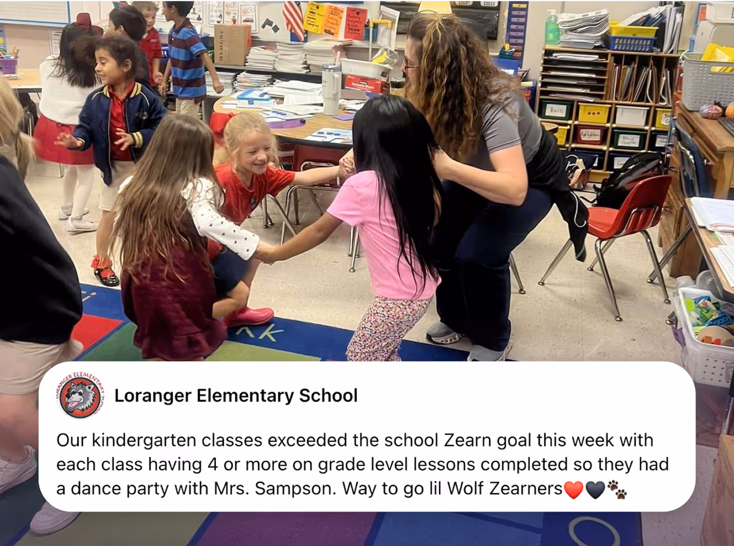 Kindergarten students at Loranger Elementary School dance and celebrate in a colorful classroom with their teacher, Mrs. Sampson. The children hold hands and smile as they enjoy a reward party for exceeding their Zearn math goals, with books, desks, and classroom supplies visible in the background.