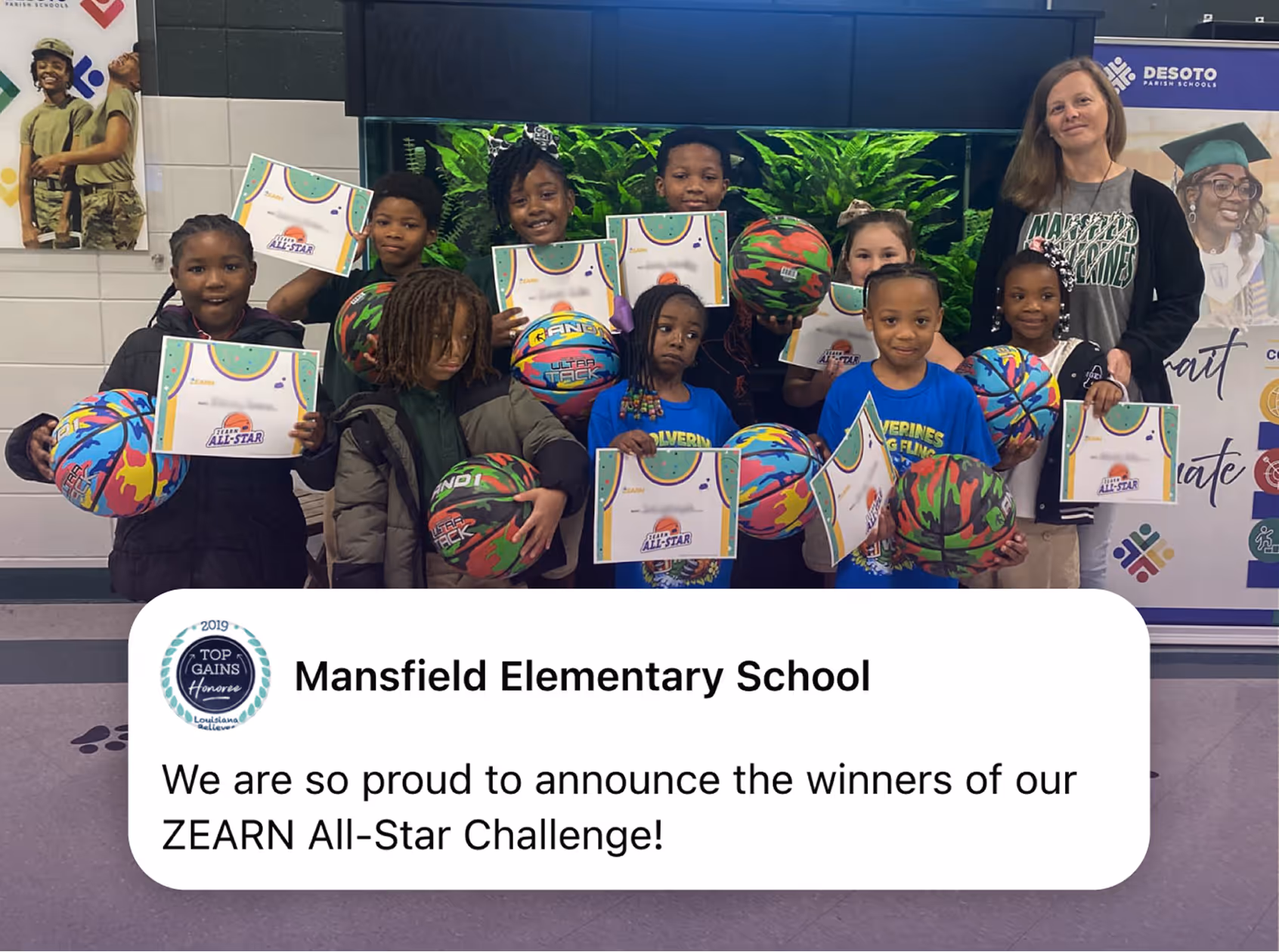 Group of elementary school students holding certificates and basketballs with an adult in a school lobby.