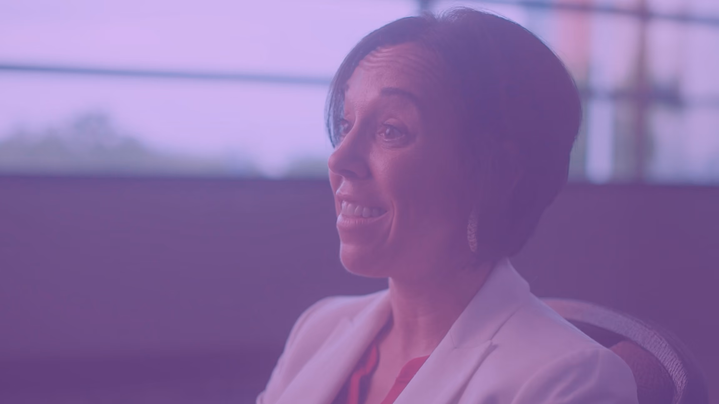 Woman with short dark hair smiles and talks while seated in a softly lit room.
