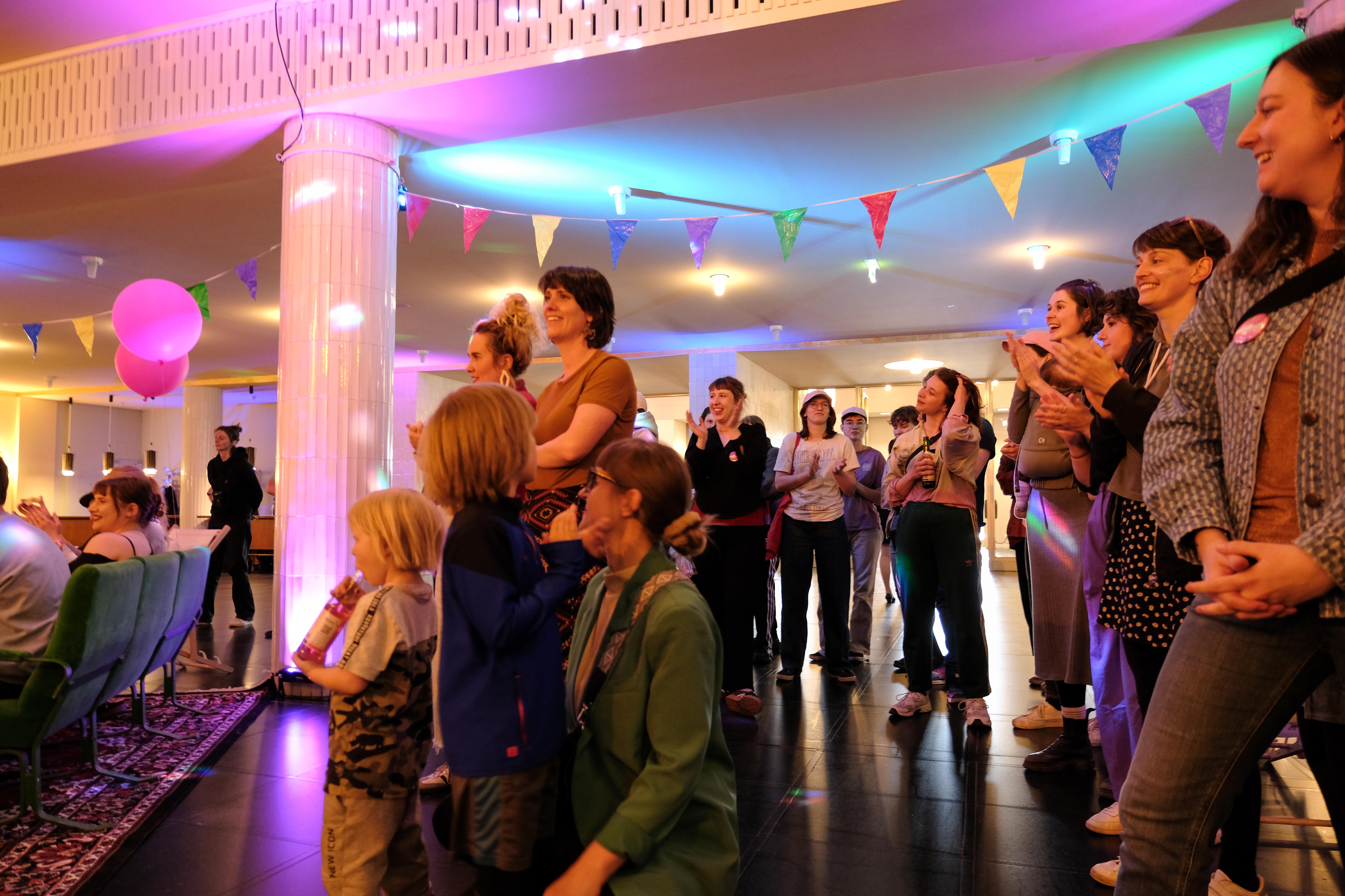 Lachende und applaudierende Menschen, Luftballons und eine bunte Girlande.