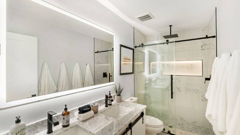 Modern bathroom with glass shower, large mirror, and marble countertop.