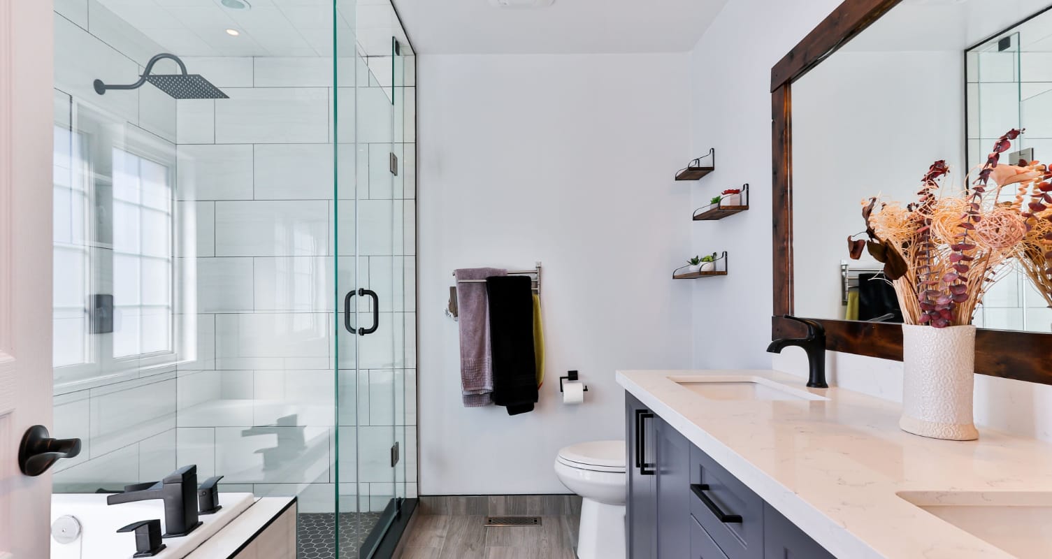 Modern bathroom with glass shower, large mirror, and dried plant arrangement.