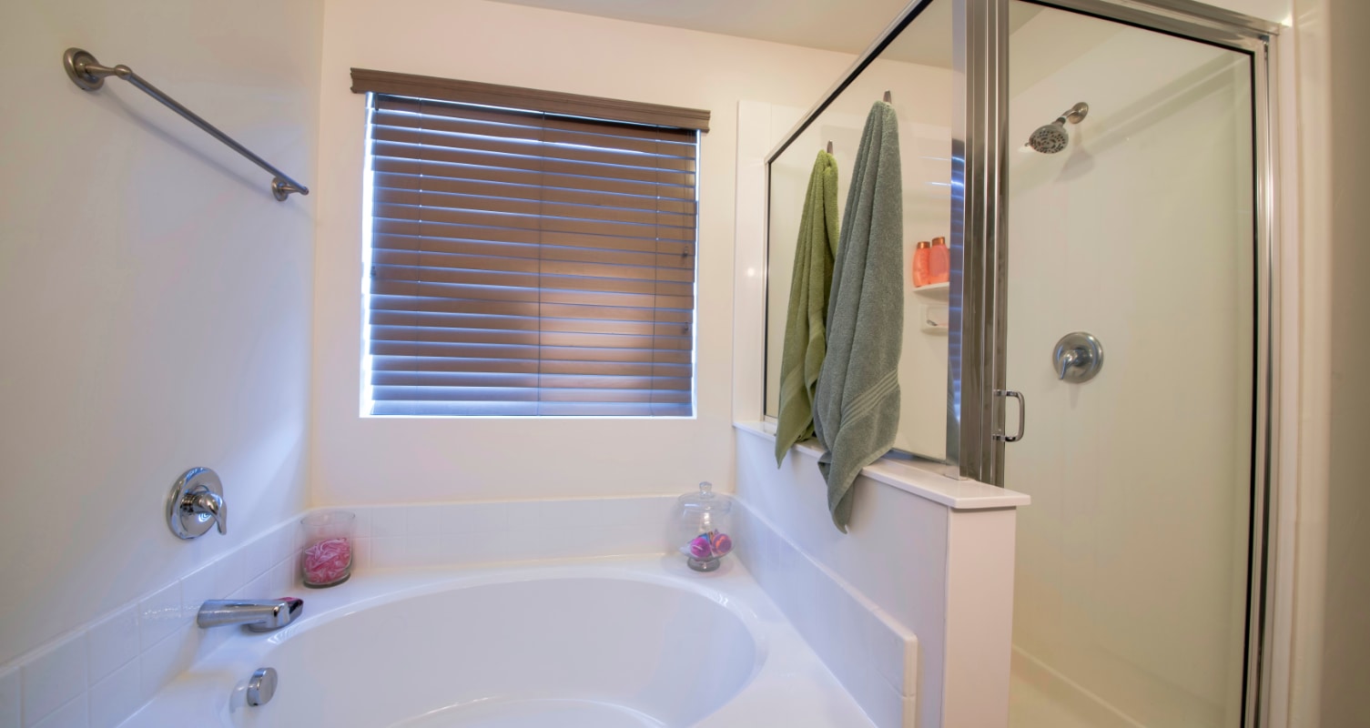 Bathtub with blinds and adjacent shower.