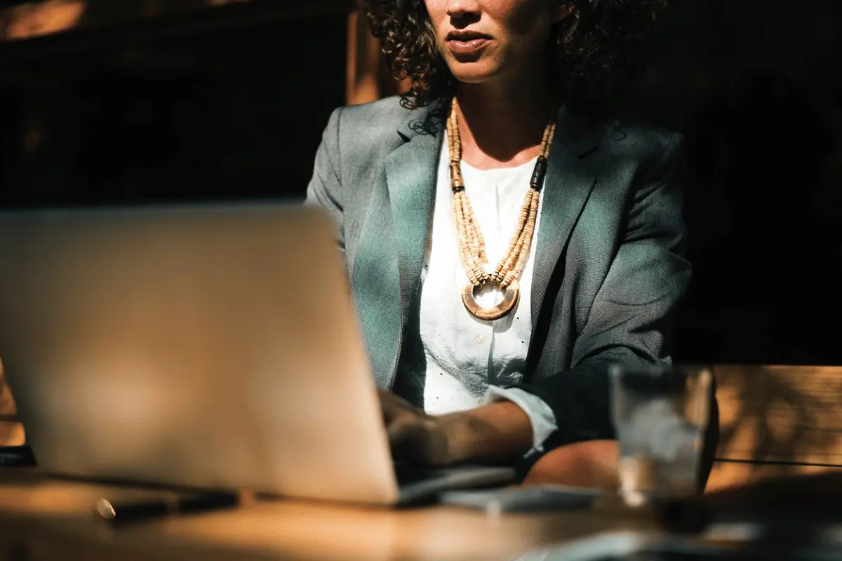 Stylish female entrepreneur with a decorative necklace using her laptop at a wooden desk.