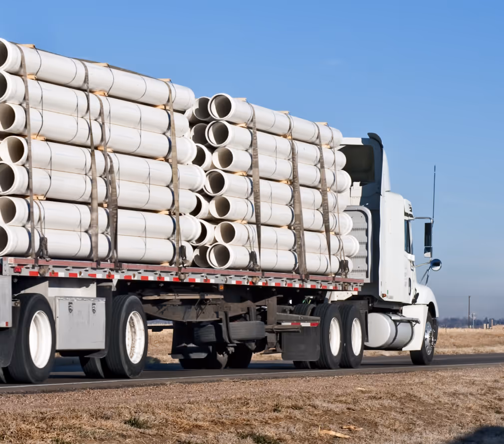 A large truck transporting stacks of white PVC pipes on a highway