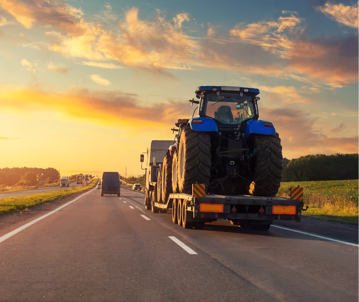 Blue tractor being transported on a trailer during sunset on a highway