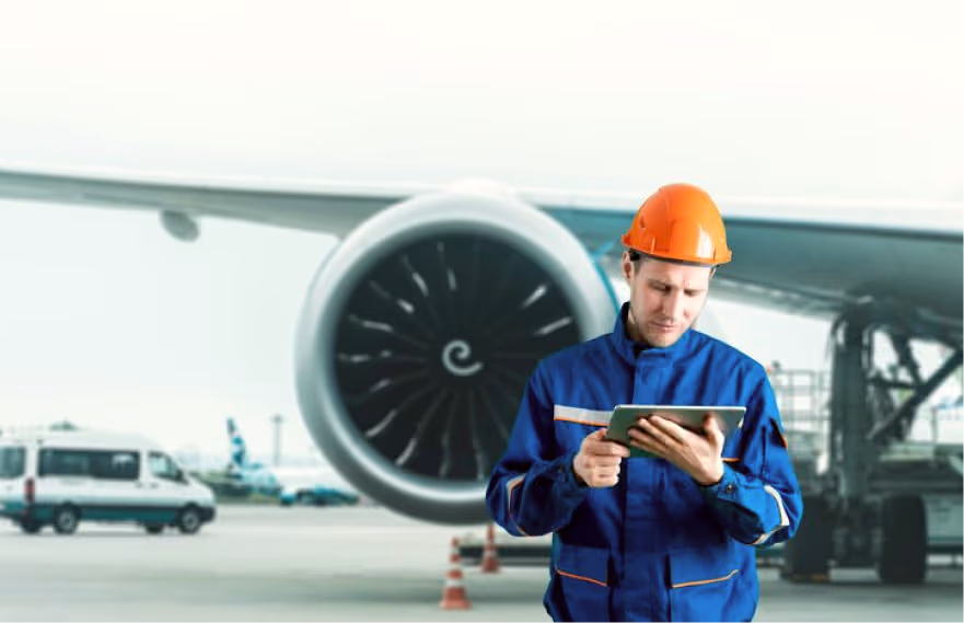 Aviation engineer in blue uniform using a tablet near an airplane engine