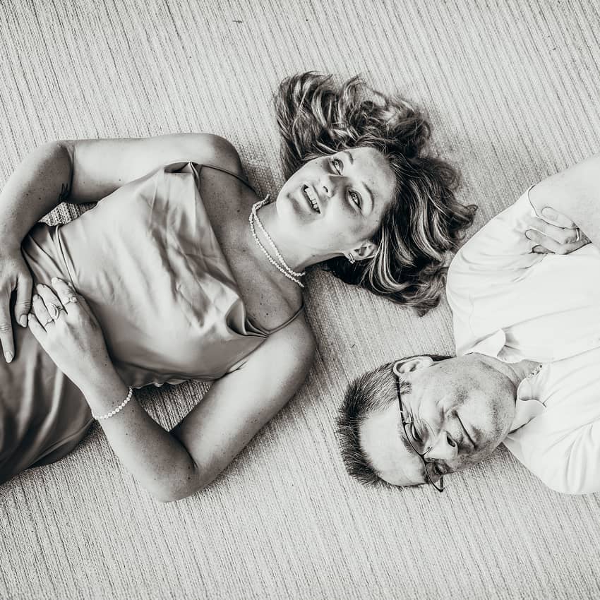 Schwarzweißfoto: Kathi Kattinger mit Perlenkette und Herbert Hutterer mit Brille liegen Kopf an Kopf lächelnd auf dem Boden.