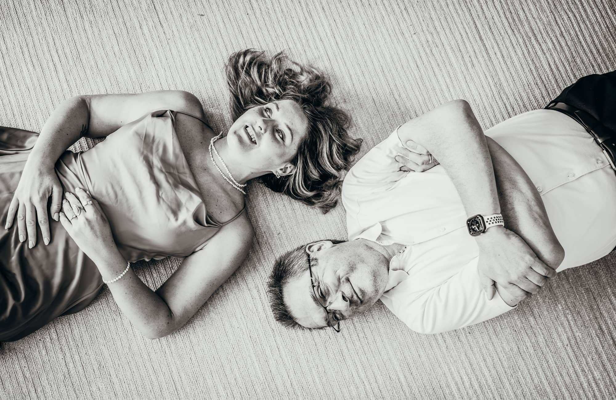Schwarzweißfoto: Kathi Kattinger mit Perlenkette und Herbert Hutterer mit Brille liegen Kopf an Kopf lächelnd auf dem Boden.