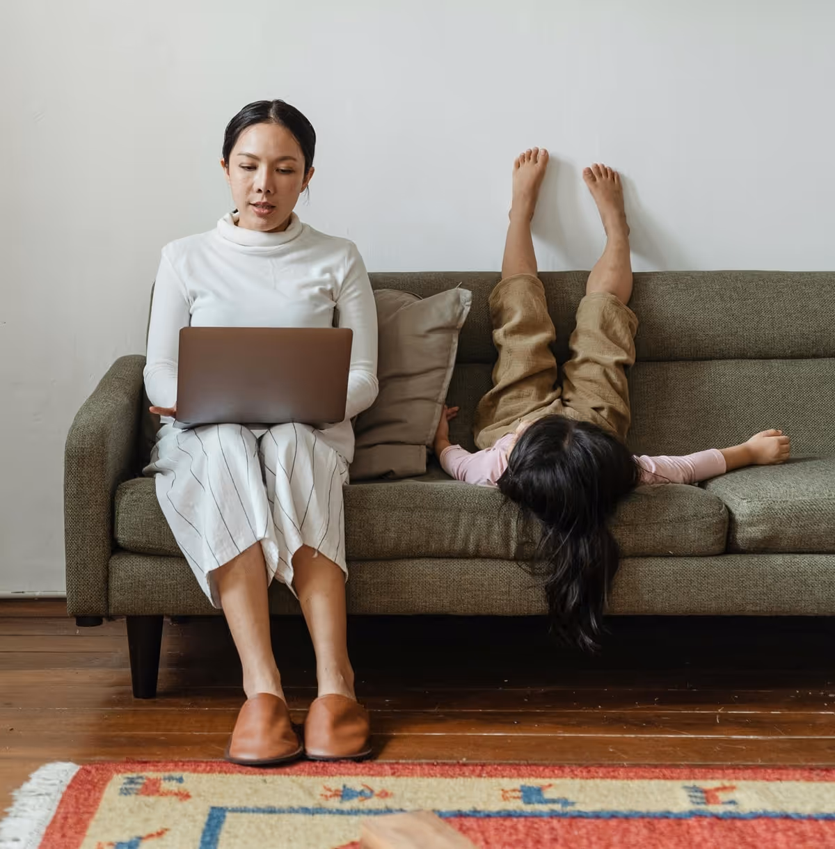 Mother working in a laptop while sitting on a couch and daughter lying on the couch