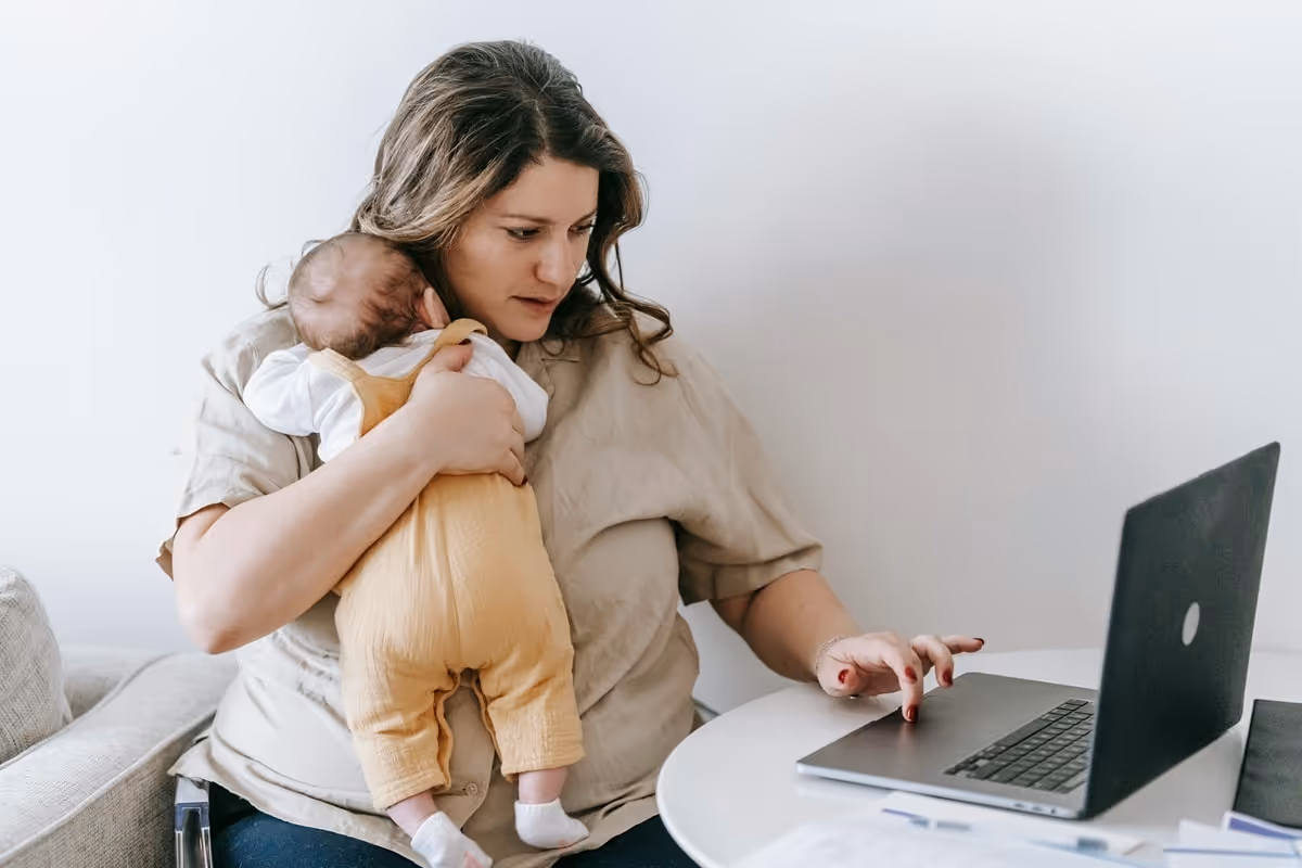 mother working on a laptop and holding her kid