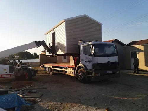 a forklift placing a prefabricated mobile house onto a truck to move it