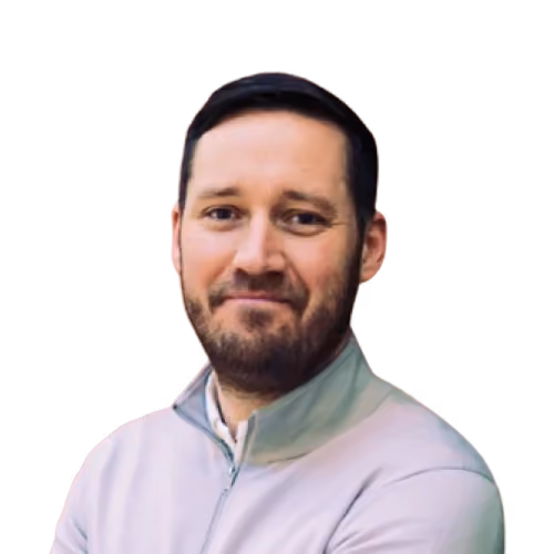 Man with beard and short dark hair wearing a light-colored zip-up sweater against a beige background.