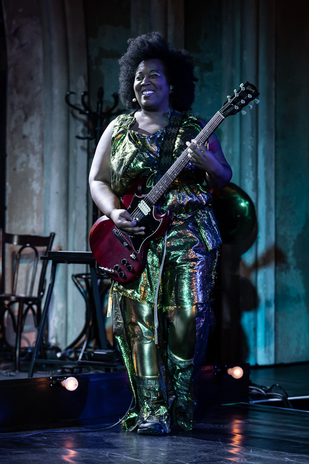 Sky Deep performing live on stage playing a red electric guitar in a gold sequined outfit.