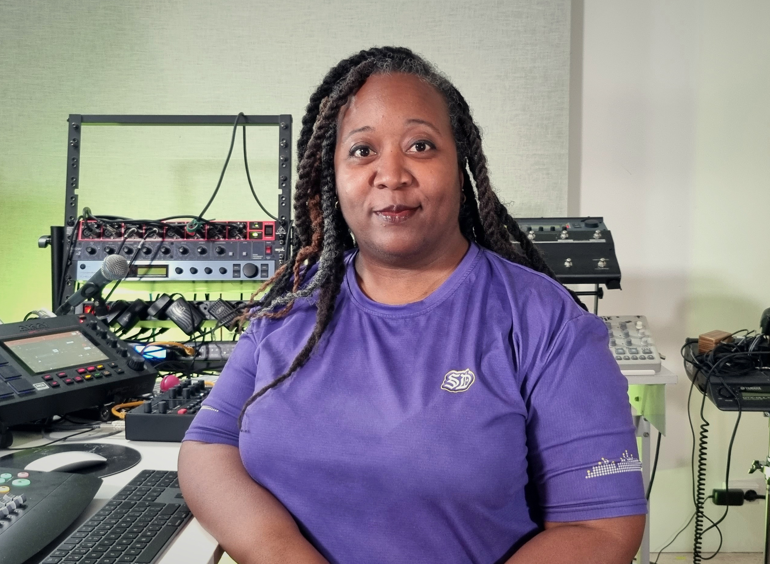 Sky Deep sitting in a professional music production studio surrounded by hardware synthesizers and gear. 