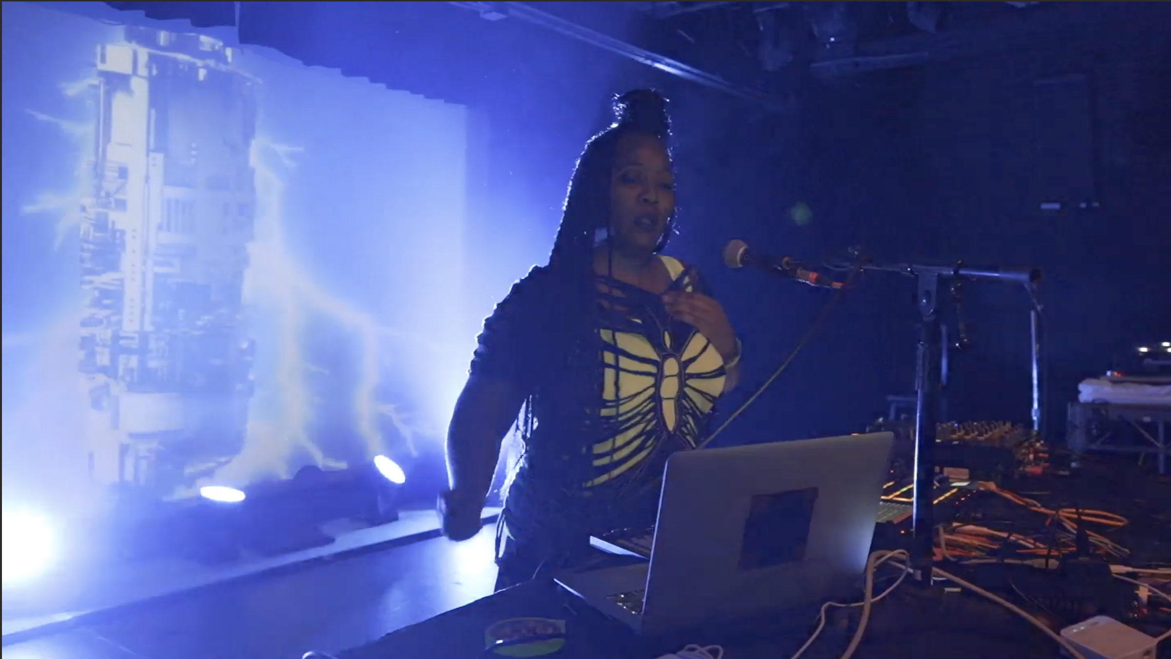 Sky Deep performing on stage with a laptop and gear, featuring dramatic blue lightning visuals in the background.