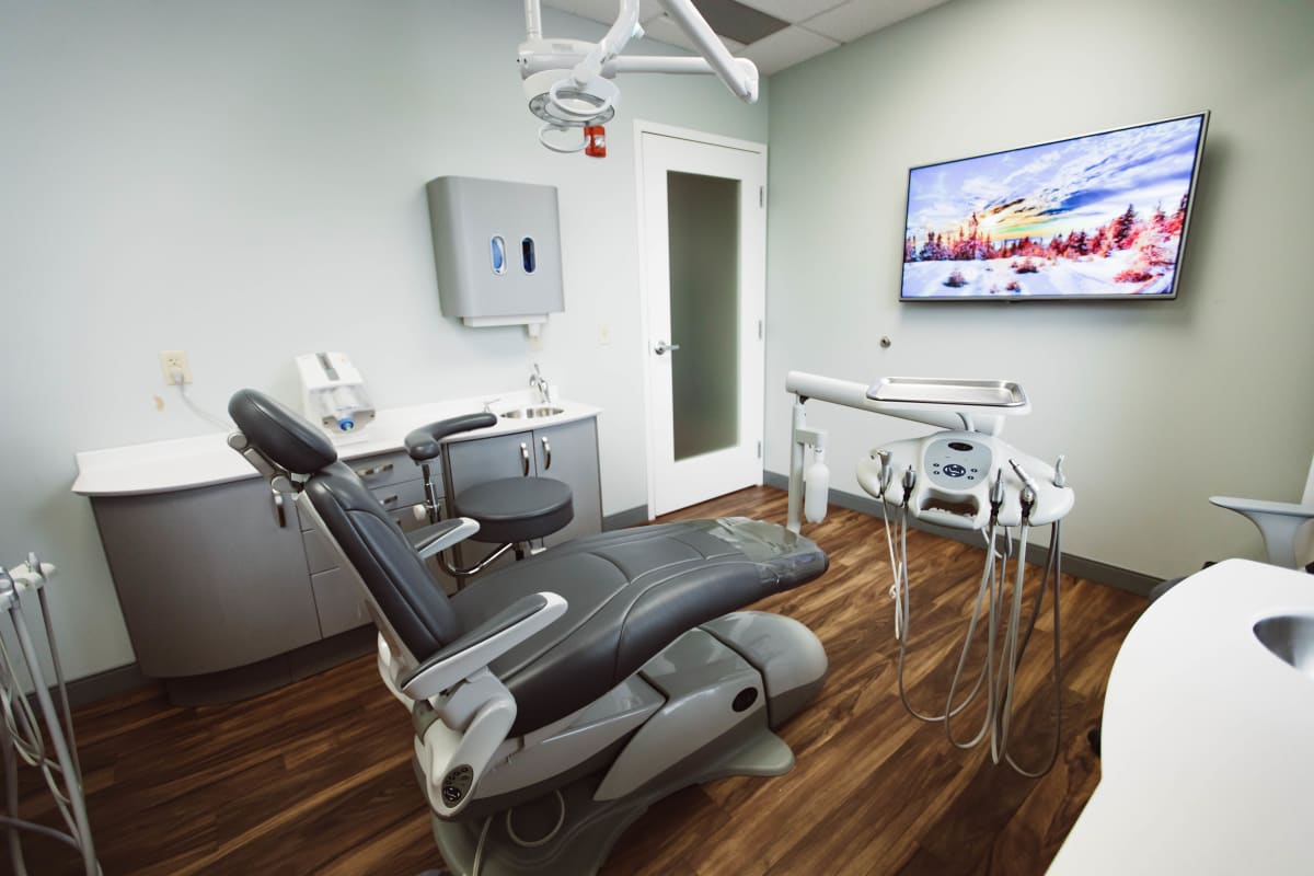 Modern dental operatory with patient chair, overhead lighting, and digital display screens