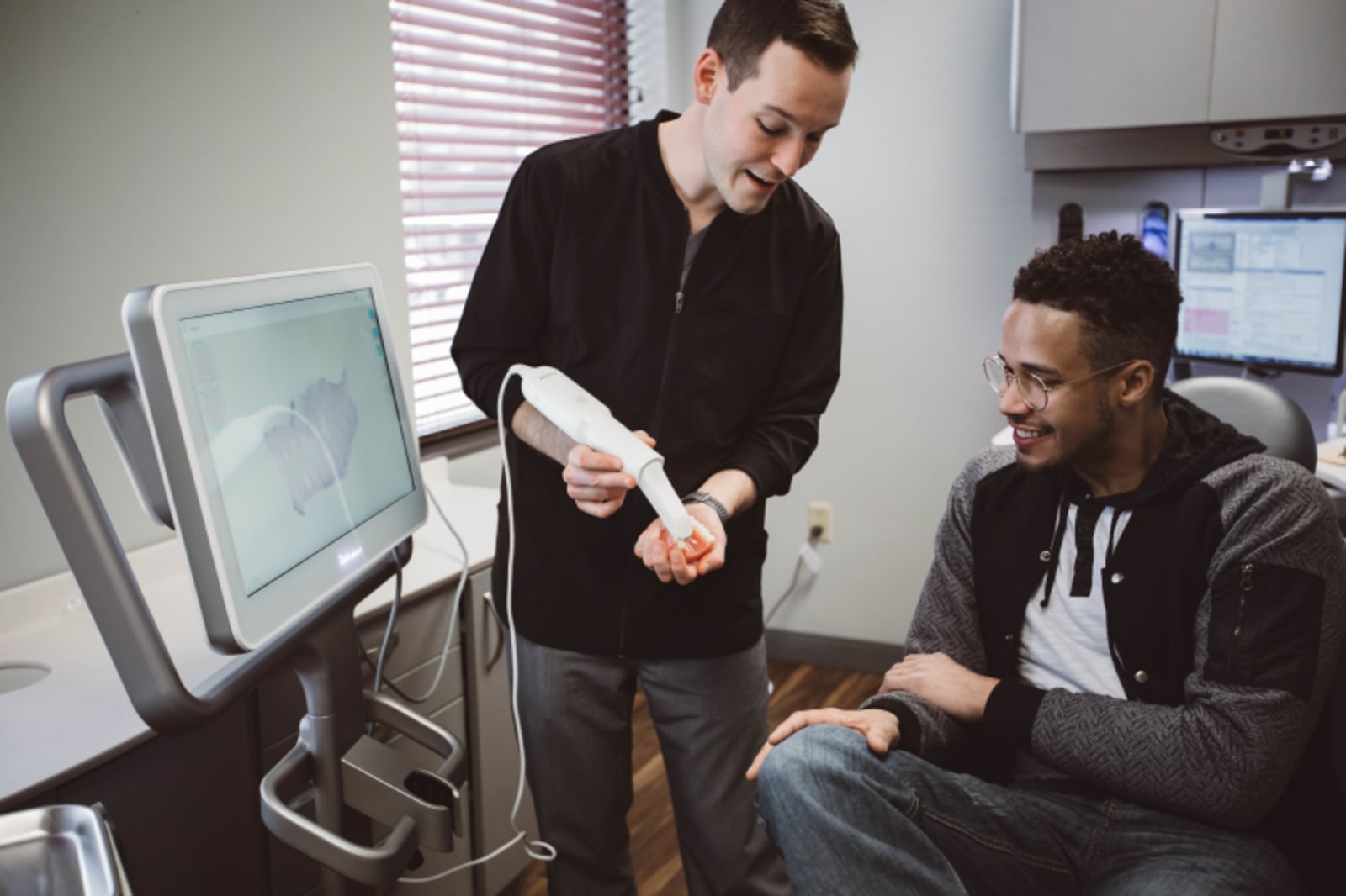 Dentist discussing fluoride treatment options with male patient in office consultation room.