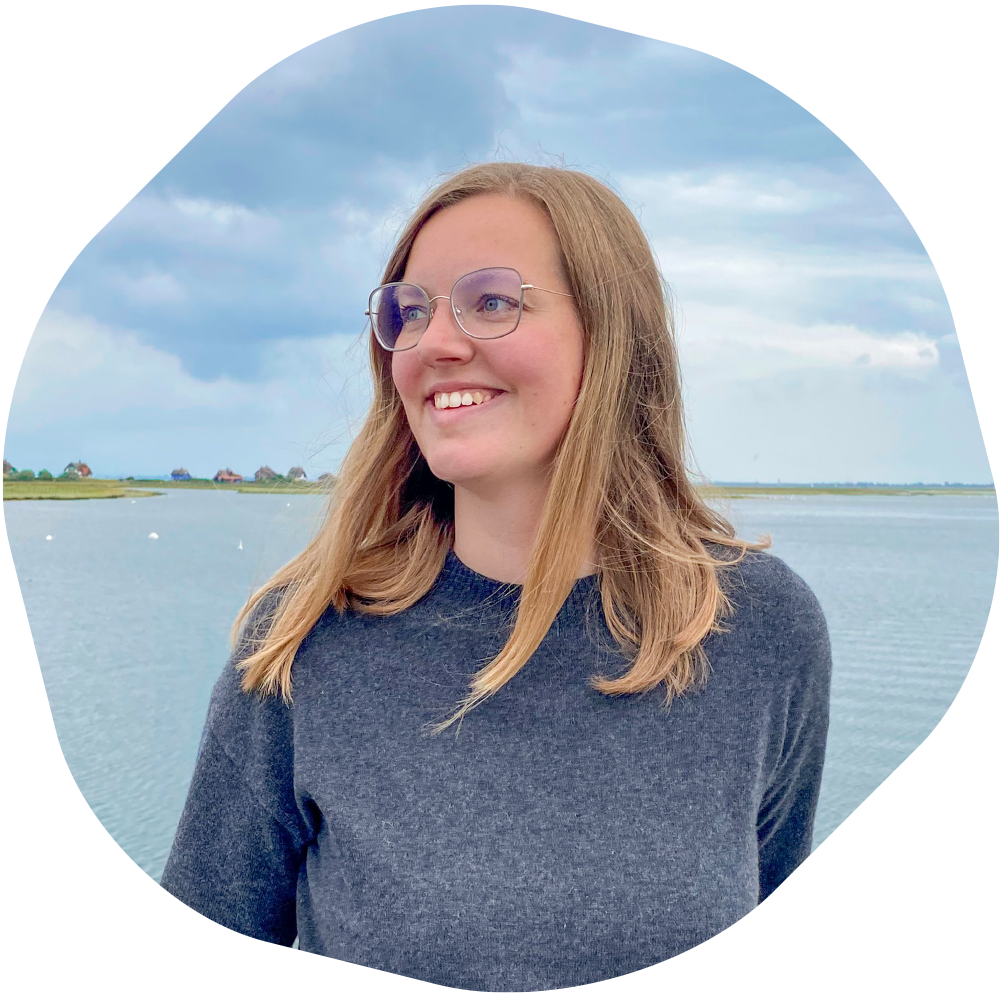 Portraitfoto Frau mit blonden schulterlangen Haaren und Brille, Meer im Hintergrund