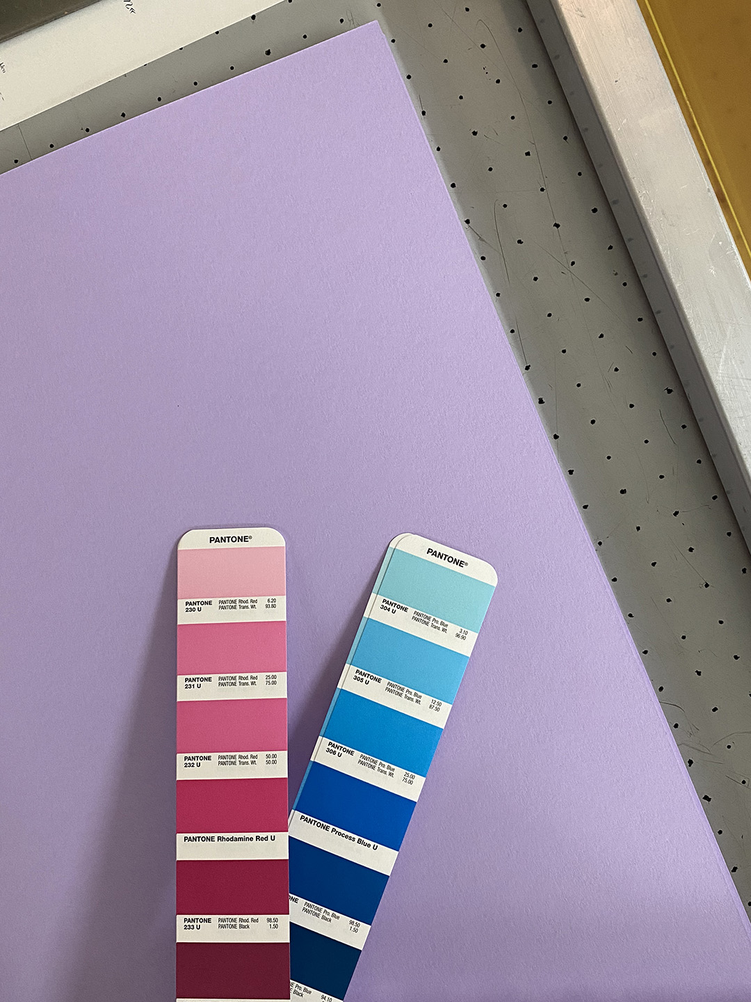 Pantone Fächer zeigt zwei Farben auf lilafarbenem Papier, Sieb und weißes Papier im Anschnitt