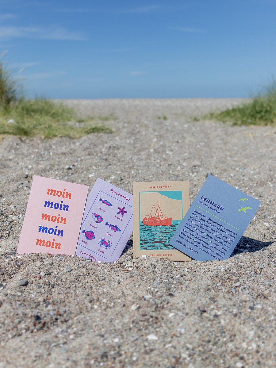 Vier bunte Postkarten mit nordischen Motiven am Strand fotografiert