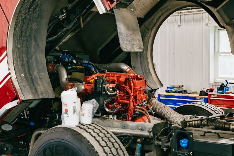 Close-up of a red diesel engine inside a semi-truck with the hood open, surrounded by tools and replacement filters. 