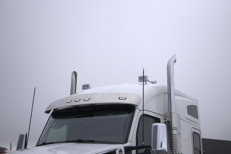 Front view of a white semi-truck cab with tall exhaust stacks, antennas, and roof lights, photographed under an overcast sky.