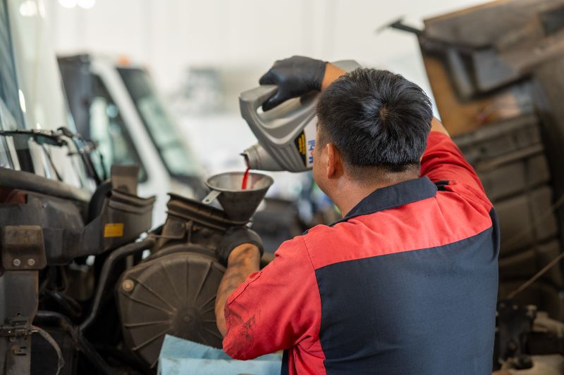 Diesel technician pouring transmission fluid into a truck engine during routine maintenance at a commercial fleet repair facility.