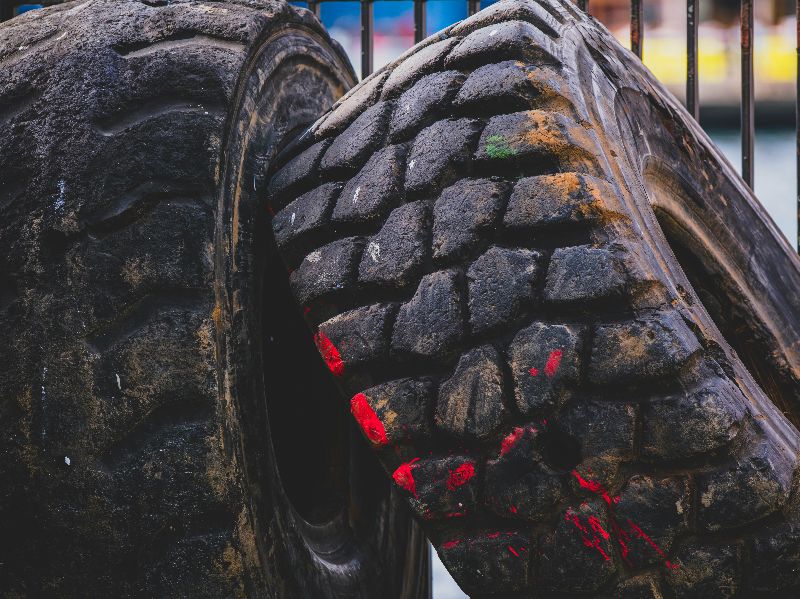 Two large worn heavy-duty truck tires leaning together, showing deep rugged tread patterns with dirt and red paint markings.