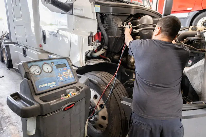 HVAC service on semi truck with technician connecting gauges to AC system using Robinair CoolTech machine for diagnostics.