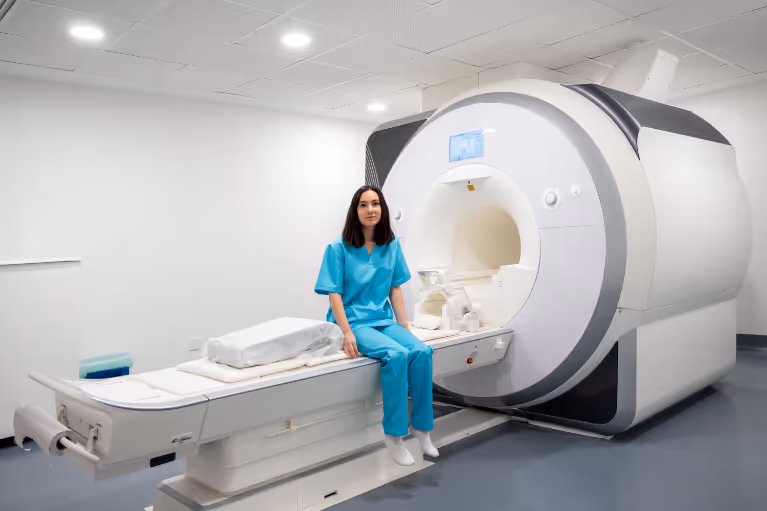 A young woman in a hospital outfit sitting on a MRI machine.