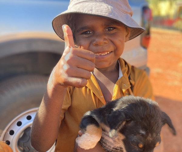 Young child holding a dog giving a thumbs up