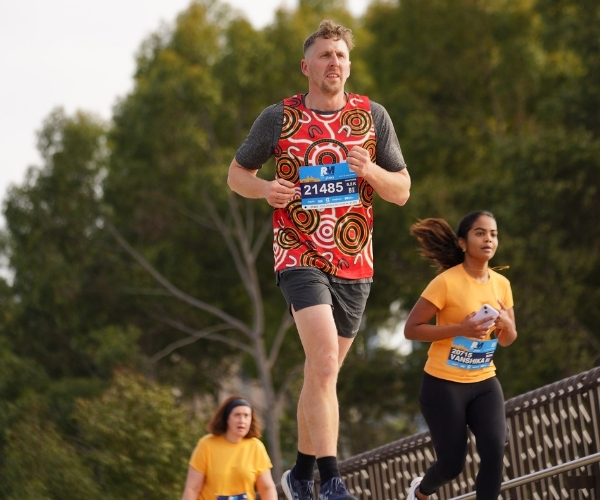 Man running in a Red Dust Running Singlet with other runners behind him