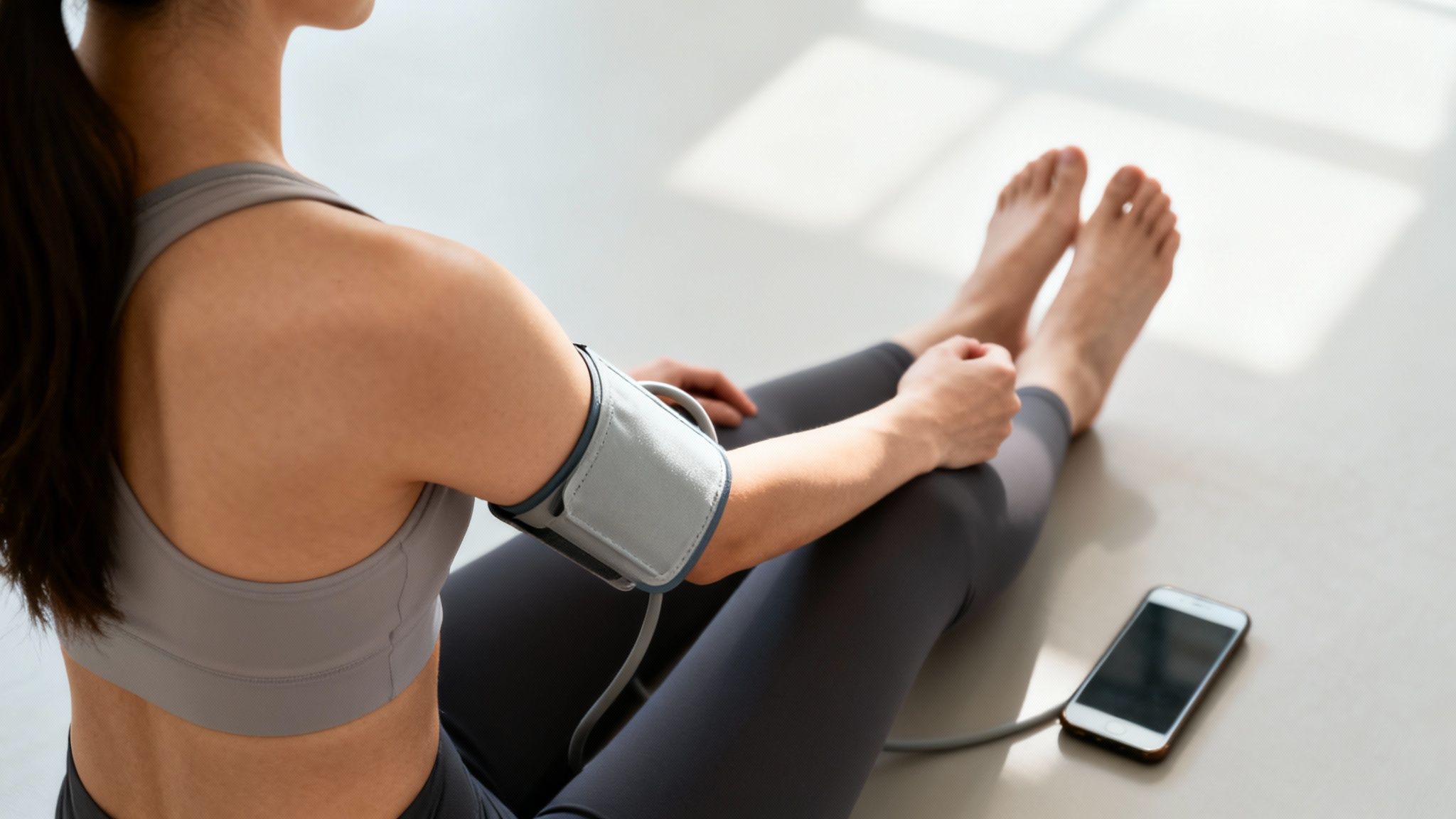 Woman sitting on the floor, measuring her blood pressure with a cuff connected to a smartphone.