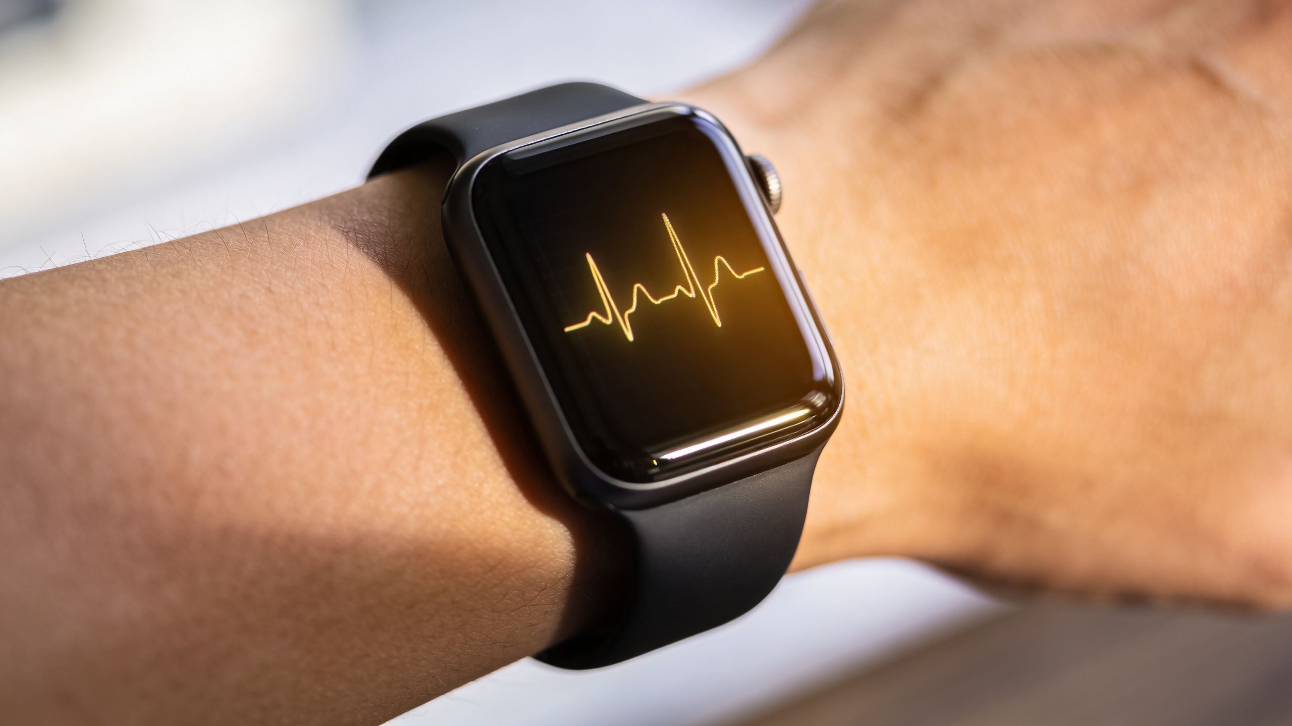 Close up view of a person wearing a black smartwatch showing a heart rate ECG monitor display.
