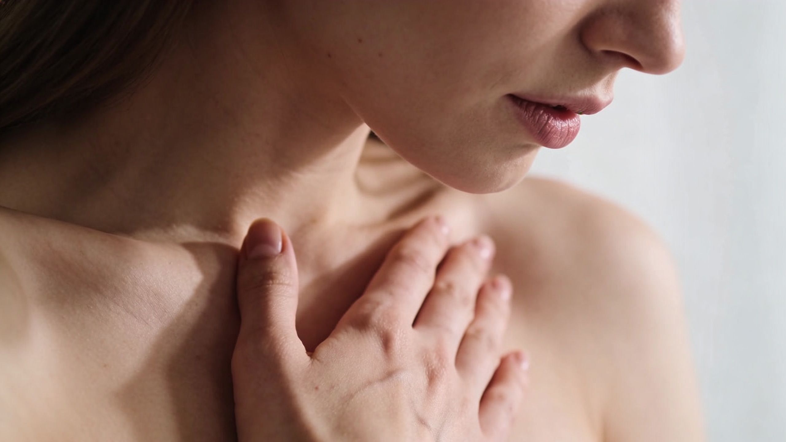 A close-up view of a woman touching her chest with her hand, suggesting discomfort or physical concern.