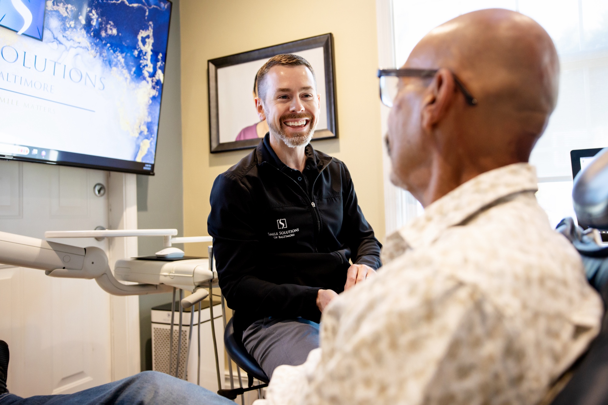 Dr. Ritter is seated, smiling and consulting with a patient in the operatory at Smile Solutions of Baltimore.