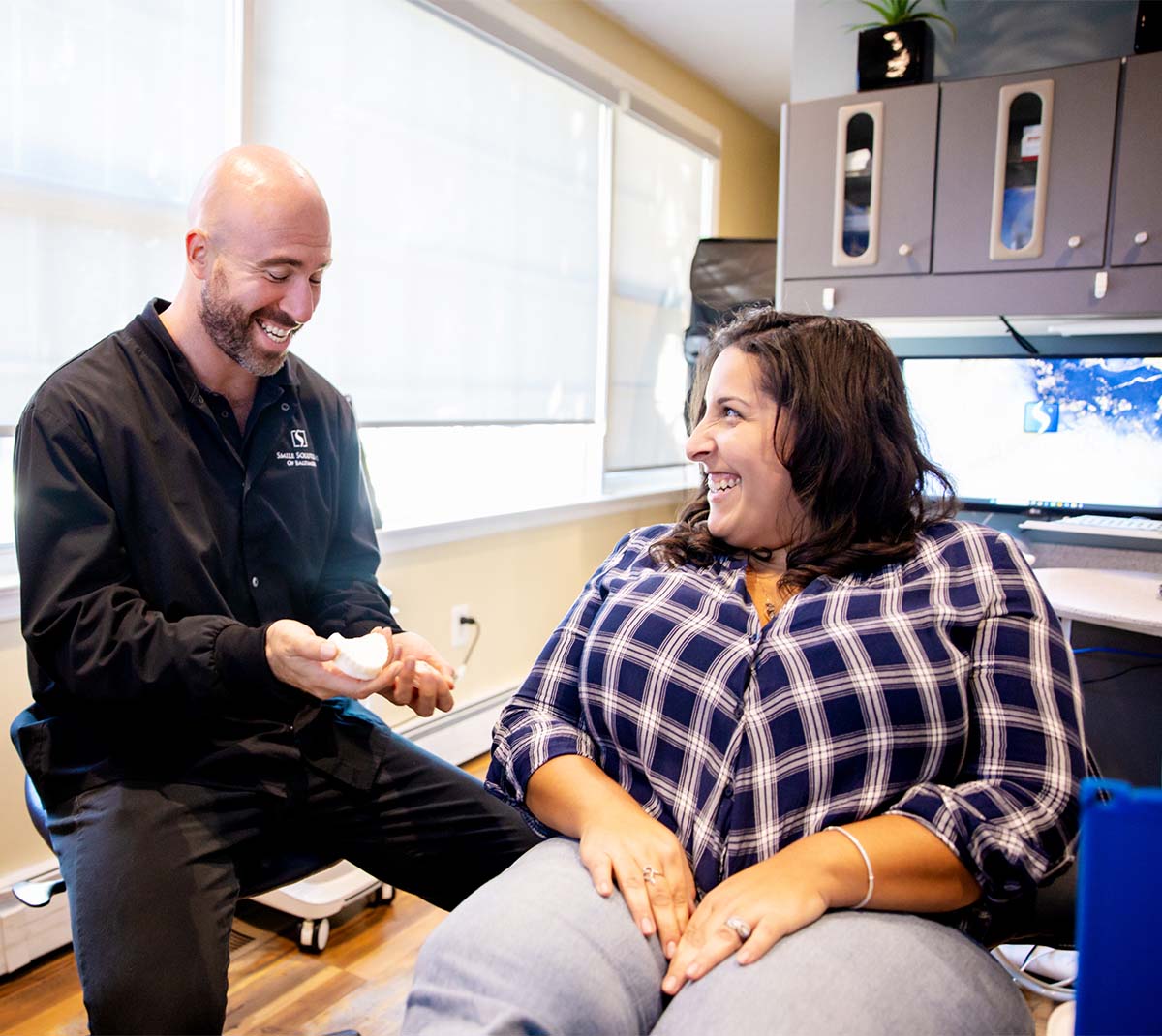 Dr. Scherr talks with a patient in the dental chair and shows her a mouth model of a cosmetic dental solution.