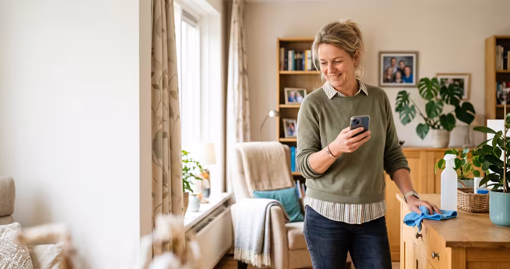 Huishoudelijke hulp leert op haar telefoon tijdens het werk in de huiskamer van een cliënt