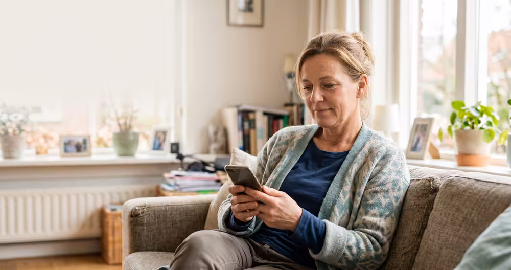Zorgmedewerker bekijkt rustig haar smartphone op de bank — veilig omgaan met digitale gegevens