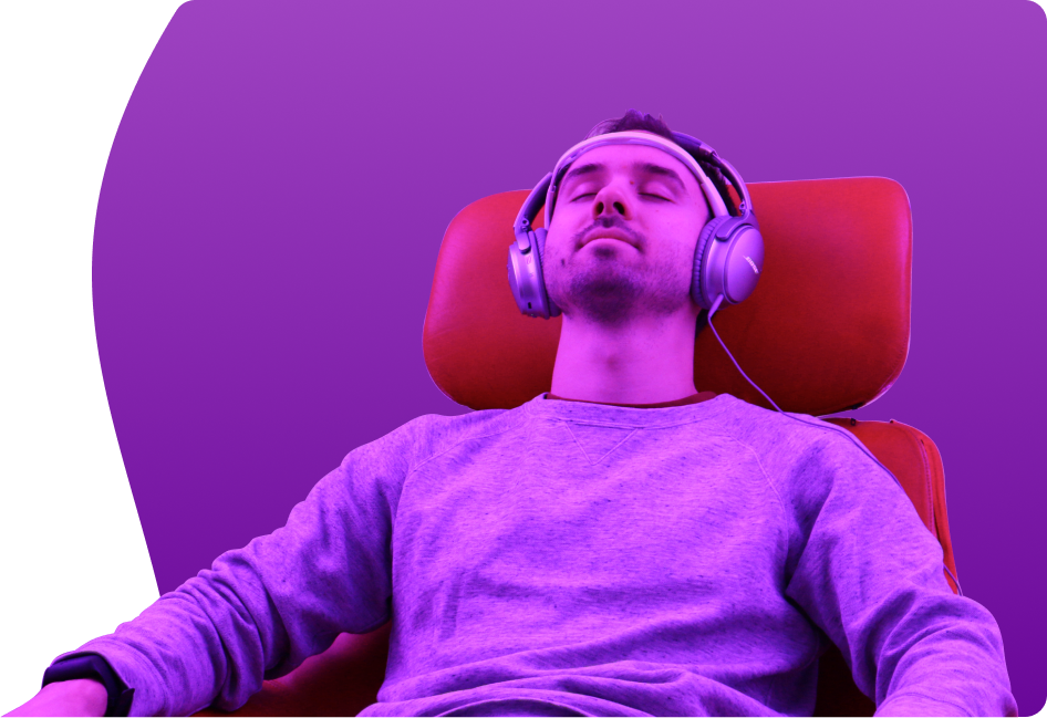 young man is listening to music in headphones relaxing in red chair