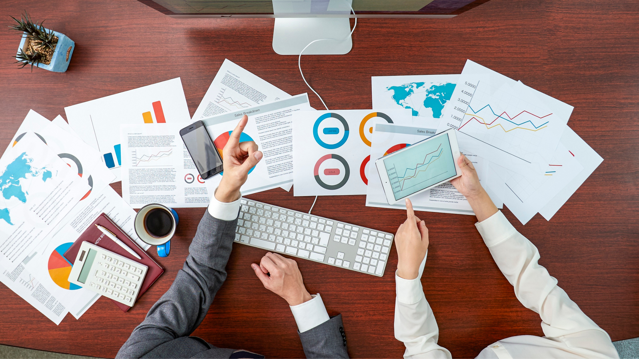 Business analytics sheets are spread out on a table while two employees point to relevant data.