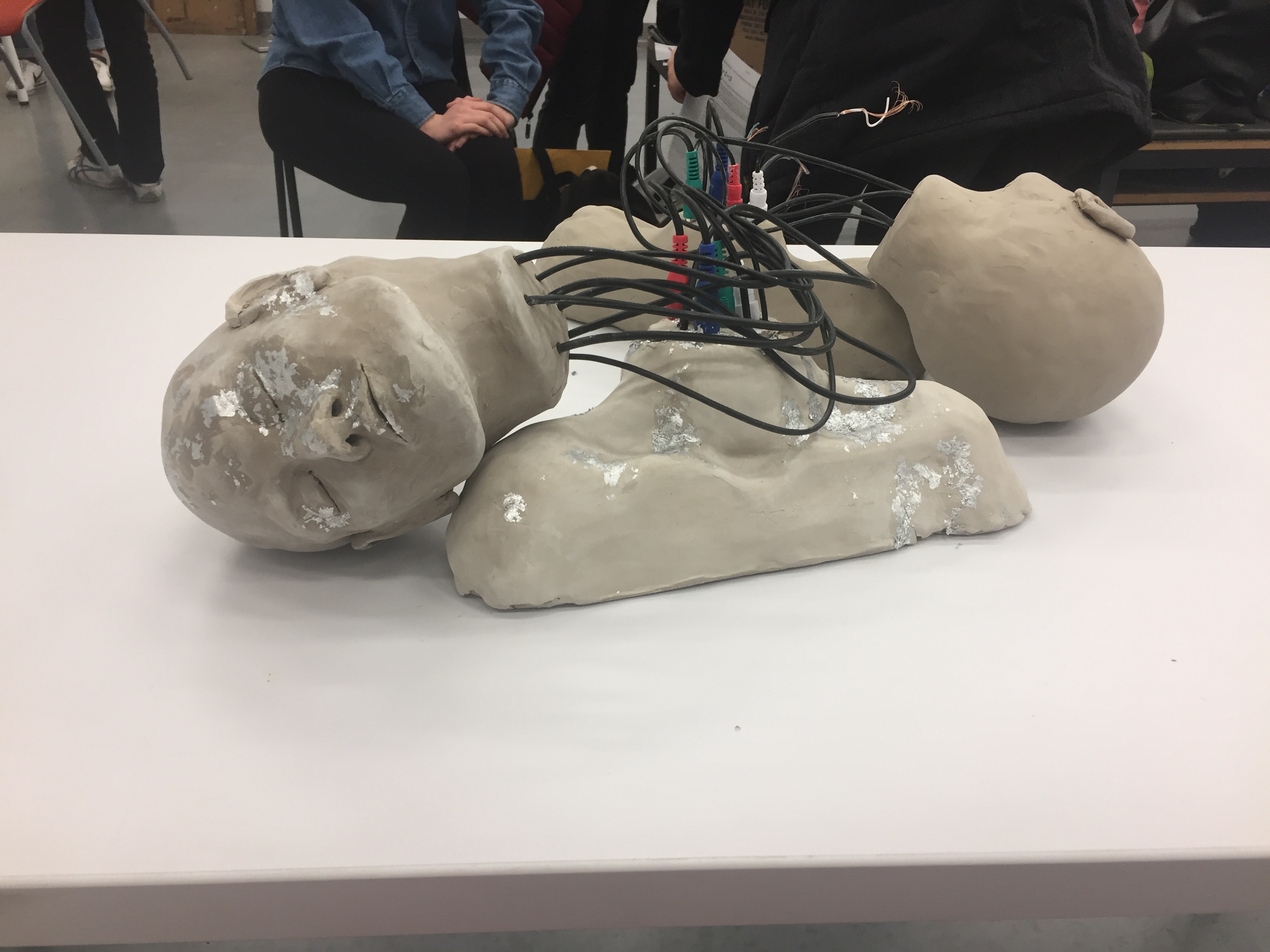 clay sculpture of two heads connected to shoulders by electrical wires